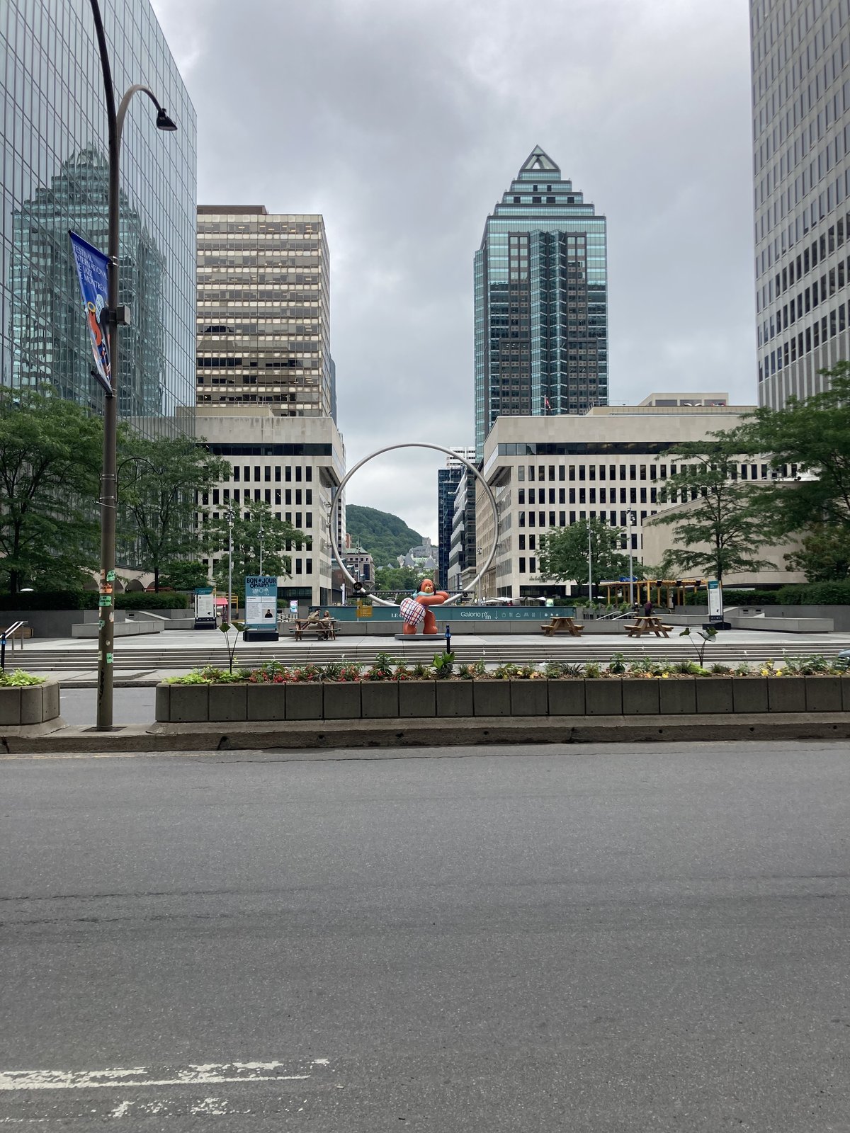 A large steel ring sculpture on a Montreal plaza framing Mount Royal in the distance between office towers.